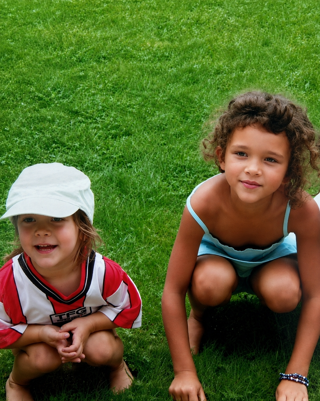 Ella and Maia as children, crouching together on a garden lawn